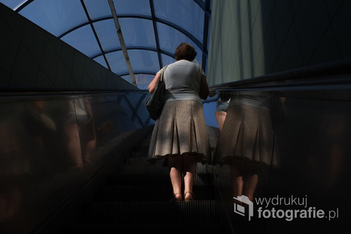 Zdjęcie zrobione w 2016 roku przy wyjściu z warszawskiego metra. Przedstawia kobietę, oraz  delikatne światło, które oświetla jej sylwetkę.
