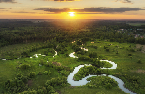 Beautiful aerial drone view of sunset over green fields and wild river
