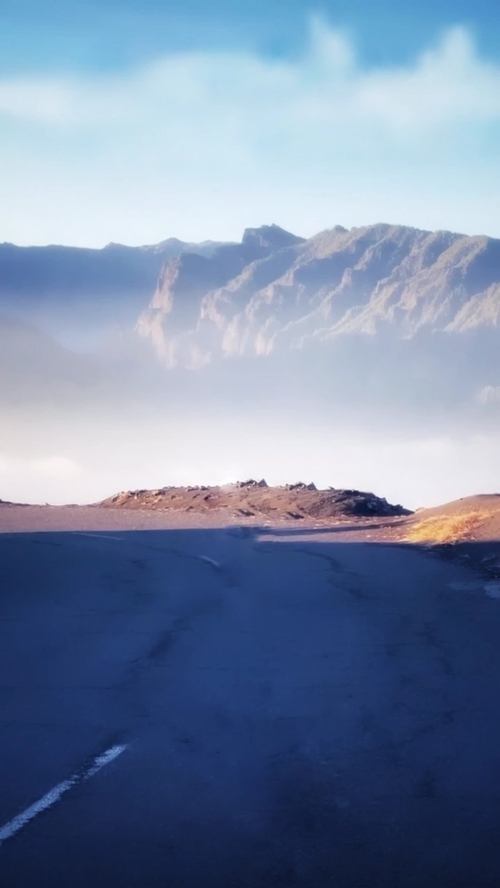 Zdjęcie przedstawia drogę oraz góry we mgle , szczególną uwagę przekuwa niebo .