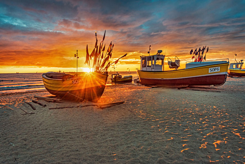 Zdjęcie zrobione o wschodzie słońca na sopockiej plaży. Na drugim planie powracający w połowu rybacy.
