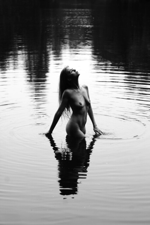 Minimalistyczna fotografia ukazująca kontrast między smukłym kobiecym ciałem a taflą wody.