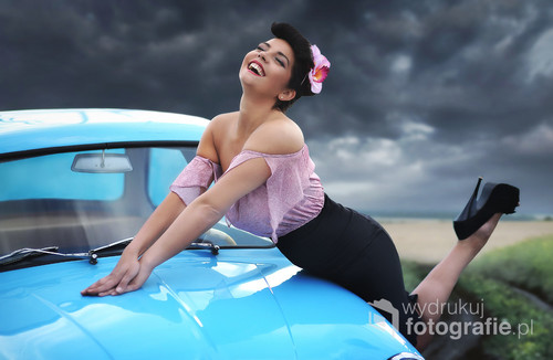 Zdjęcie przedstawia młodą kobietę w stylizacji pin-up na tle samochodu marki Syrenka i zajęło I miejsce w konkursie 