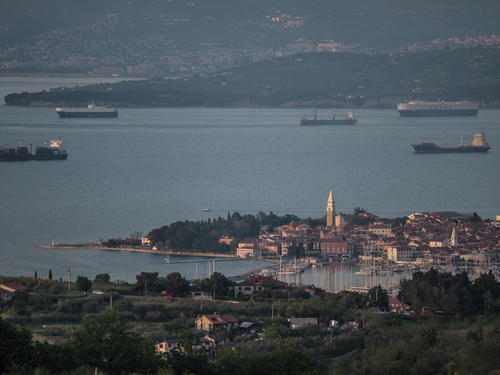 To zdjęcie ukazuje malowniczą panoramę miasta Izola, położonego na wybrzeżu Adriatyku w Słowenii. Zostało ono wykonane z widokowego punktu na wzgórzu, co pozwala na zachwycanie się pięknem tego miejsca z perspektywy ptaka. Zachód Słońca dodaje jeszcze większego uroku temu widokowi.

Na pierwszym planie rozciąga się imponujący widok na miasteczko Izola, które błyszczy setkami światełek. Urocze uliczki, zabytkowe budowle i klimatyczne kawiarnie nadają miastu niepowtarzalny urok.

W oddali rozpościera się wybrzeże Adriatyku, którego spokojne wody odbijają złociste promienie zachodzącego Słońca. Statki oczekują na wpłynięcie do portu, tworząc malowniczy kontrast do naturalnego piękna morza.

To niezapomniane zdjęcie jest doskonałą ilustracją harmonii między naturą a architekturą, jaką oferuje Izola. Widok ten w czasie zachodu Słońca podkreśla romantyczną atmosferę tego miejsca, przyciągające turystów i podróżników z całego świata.
