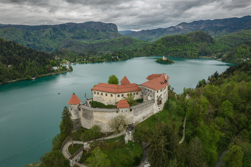 Zamek Bled to urokliwa i historyczna twierdza, położona na skalistym wzgórzu nad jeziorem Bled w Słowenii. Jest to fascynujący przykład architektury obronnej, którego korzenie sięgają średniowiecznych czasów, a który od lat przyciąga turystów z całego świata.

Zamek ten wznosi się dumnie nad jeziorem Bled i jest otoczony malowniczymi Alpami Julijskimi, tworząc niezwykle widok. Jest to miejsce, które emanuje historią i tajemnicą, ponieważ jego początki sięgają XII wieku. W ciągu wieków pełnił różne funkcje, w tym obronne, rezydencjonalne i administracyjne.

Charakterystyczną cechą Zamku Bled jest jego architektura, z kamiennymi murami, wieżą i dziedzińcem wewnętrznym. Wewnątrz zamku można zobaczyć liczne sale i wystawy muzealne, które opowiadają historię regionu i zamku. Jednym z najbardziej urokliwych miejsc w zamku jest dziedziniec, z którego rozciągają się wspaniałe widoki na jezioro Bled i okoliczne góry.

Zamek Bled to także doskonałe miejsce na relaks i odpoczynek. Można tu zjeść tradycyjne słoweńskie potrawy w restauracji zamkowej lub spacerować po urokliwym parku wokół zamku.

Odwiedzając Zamek Bled, można nie tylko odkryć historię Słowenii, ale także podziwiać niezwykłą scenerię, która towarzyszy temu urokliwemu miejscu. To jedno z najważniejszych i najbardziej rozpoznawalnych miejsc w Słowenii, które pozostawi niezapomniane wrażenia i zachwyci każdego miłośnika historii oraz piękna przyrody.