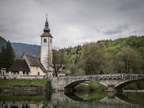 To magiczne zdjęcie ukazuje urok i spokój nad pięknym jeziorem Bohnijskim na Słowacji. Na pierwszym planie widać wspaniały kamienny most, który jest prawdziwym świadectwem historycznej architektury i stanowi nieodłączną część krajobrazu tego miejsca.

Nieopodal wznosi się majestatycznie Cerkev Sv. Janeza Krstnika, czyli Cerkiew Świętego Jana Chrzciciela. Jego wieża i dachy kryty tradycyjnymi drewnianymi gontem tworzą wyjątkowy widok na tle górskiego pejzażu. Ta cerkiew to prawdziwa perła architektoniczna, która jest zarazem symbolem ducha i kultury tego regionu.

Jezioro Bohnijski jest niewątpliwie jednym z najpiękniejszych miejsc na Słowacji. Góry otaczające jezioro, odbijające się w spokojnej taflę wody, tworzą magiczną atmosferę spokoju i kontemplacji. To miejsce jest idealne zarówno dla miłośników przyrody, jak i tych, którzy pragną zanurzyć się w historii i kulturze tego regionu.

To zdjęcie nad jeziorem Bohnijskim przenosi nas w czasie i przestrzeni, ukazując piękno przyrody i kultury Słowacji w jednym spojrzeniu. To miejsce jest prawdziwym skarbem, który warto odkryć i docenić.