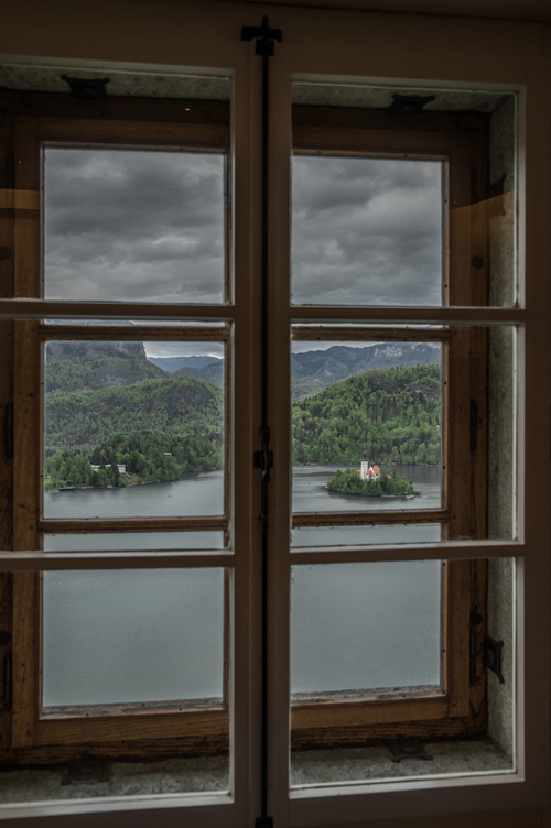 Ikoniczna wysepka na Jeziorze Bled z okna Zamku Bled. Z tej niecodziennej perspektywy ukazuje się prawdziwa perła krajobrazu Słowenii. Okno tworzy swoistą ramkę otaczającą wyjątkową scenę, tworząc niepowtarzalny widok na malowniczą wysepkę na Jeziorze Bled.

W oddali, na środku jeziora, znajduje się ikoniczna wysepka z malowniczą cerkwią, która jest jakby sercem tego zakątka. Woda jeziora Bled o spokojnej tafli tworzy idealne otoczenie wskazując co w tym miejscu najbardziej przykuwa uwagę.

Okno zabytkowego zamku, noszące ślady długiej historii, stanowi idealne obramowanie dla tej niezwykłej scenerii. To miejsce emanuje historią i tajemnicą, ponieważ zamek sam w sobie ma długą przeszłość sięgającą średniowiecza.

To zdjęcie jest prawdziwym hołdem dla harmonii między człowiekiem a naturą, gdzie historia i krajobraz splatają się w jedną niezapomnianą kompozycję. Wyraża spokój, piękno i urok Słowenii, której sercem jest to malownicze jezioro z wyspą i zamkiem, tu, widziane przez magiczny ramy okna.