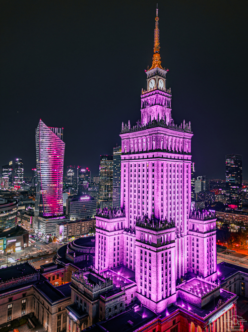 Zdjęcie wykonane z perspektywy drona, ukazuje ten znany symbol Warszawy w zupełnie nowej odsłonie. Różowe światło nadaje budowli nierealny, wręcz magiczny charakter, a jego odbicia w szklanych fasadach otaczających go budynków oraz w cichych wodach pobliskich fontann tworzą hipnotyzujący efekt. Ciemne tło nocnego nieba doskonale kontrastuje z jaskrawymi światłami miasta, nadając kompozycji głębię i dramatyzm. To zdjęcie zostało docenione i wyróżnione na wielu renomowanych stronach poświęconych fotografii i architekturze. Jest idealnym wyborem dla kolekcjonerów i miłośników unikatowych ujęć miejskich, a także stanowi wyjątkowy element dekoracyjny dla tych, którzy cenią sobie połączenie nowoczesności i historii w sercu Polski.
