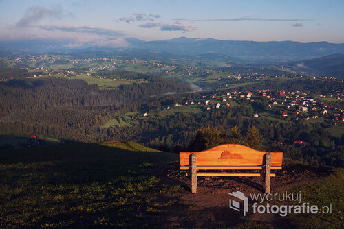 Na pierwszym planie ławeczka znajdująca się w Koniakowie na szczycie Ochodzitej. Genialny punkt widokowy i miejsce by odpocząć.
