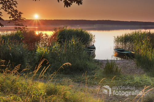 Jezioro podczas wschodu słońca latem. Na brzegu zacumowane łódki w bezpiecznej przystani pomiędzy trzcinami.