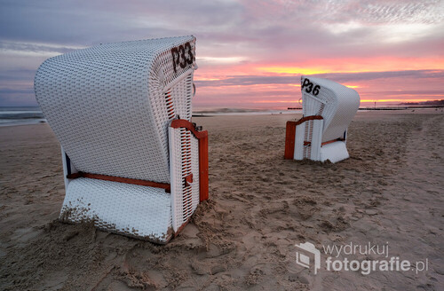 Letni wschód słońca nad plażą w Kołobrzegu. Kosze plażowe czekają, na spragnionych wypoczynku turystów.