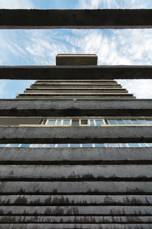 Fotografia z cyklu Warszawski Modernizm - Detale. 
Zdjęcie przedstawia brutalistyczny blok mieszkalny, widziany przez betonowe przyziemie. Budynek został zaprojektowany przez dwóch architektów, Jana Bogusławskiego oraz Bohdana Gniewiewskiego i został oddany do użytku w 1976 roku.