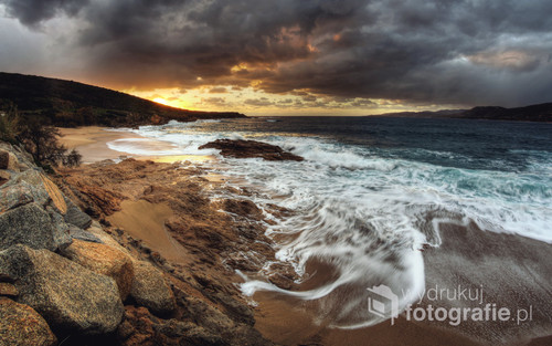 Fotografia pokazująca zachód na plaży w miejscowości Propriano, na południu Korsyki, przy wzburzonym morzu, oraz niebem pokrytym ciemnymi, burzowymi chmurami. 