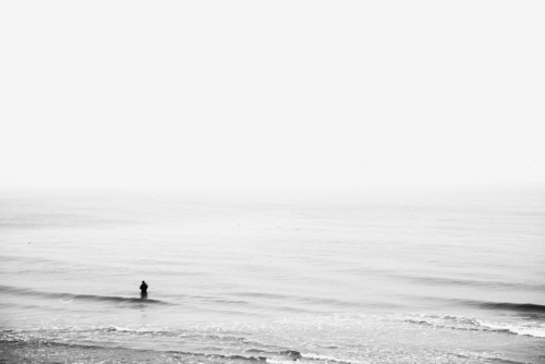 Fotografia przedstawia stojącego w morzu wędkarza. 