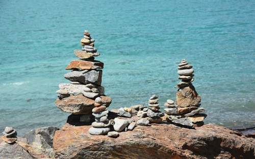 Równoważenie sztuki naskalnej. kamienie balansują jeden na drugim na kamieniu. Kamienie zen lub stos zen na tle błękitnej wody. Zdjęcie zrobione  w Południowym Tyrolu.