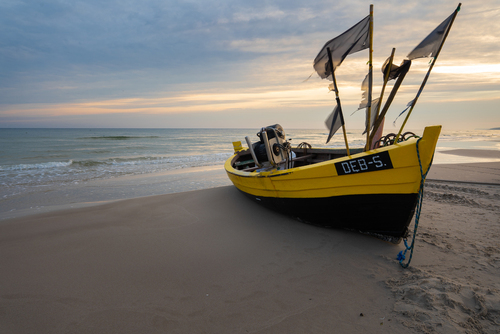 Zdjęcie wykonane na plaży w Dębkach. Przedstawia łódź rybacka kilka minut po wschodzie słońca. 