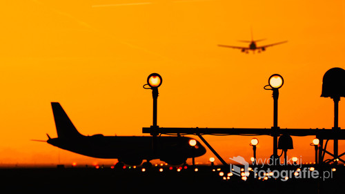 Zdjęcie przedstawia początek wielkiej przygody. Dwa samoloty, jeden kołujący na pas startowy, a drugi tuż po starcie wiozący ludzi w odległe, może jeszcze nieznane miejsce. Niesamowity klimat zachodzącego słońca wprowadza w spokojny nastrój.