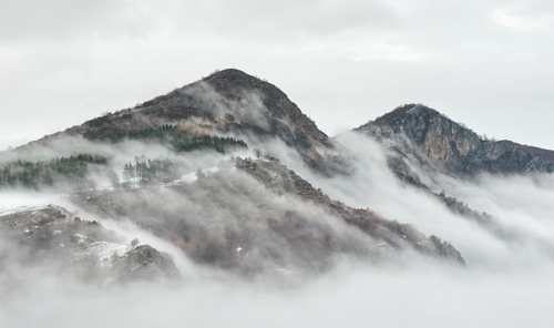 Zdjęcie przedstawia pokryte śniegiem wierzchołki pasma górskiego Stara Płanina w Bułgarii we mgle. Szczyty widoczne z miejscowości Zgorigrad.