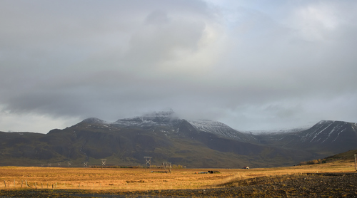 Widok na pola góry w drodze do wodospadu Glymur na Islandii. Połączenie delikatnego światła słonecznego na pierwszym planie i zachmurzonego, ponurego szczytu dodaje tej fotografii dramaturgii.