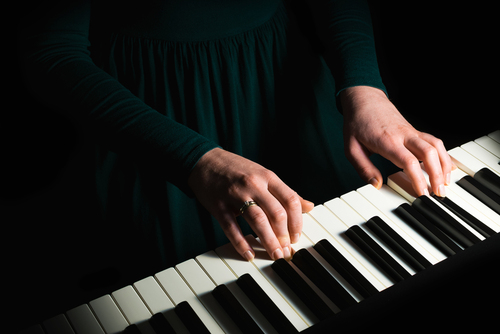 Kobieta grająca na pianinie przy kontrastowym, punktowym świetle.