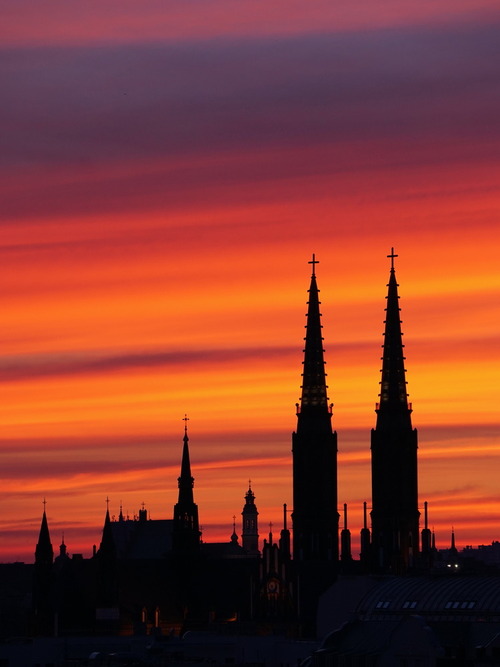Sylwetki wież katedry św. Floriana Męczennika i św. Michała Archanioła na warszawskiej Pradze-Północ na tle pasów chmur zabarwionych ciepłymi kolorami zachodzącego słońca.