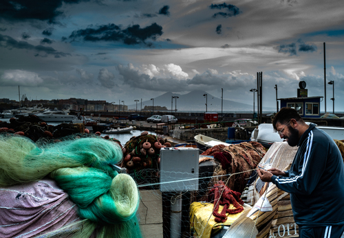 Neapol, Italia. 2019 r.
Rybak w porcie rybackim w Neapolu czyści sieci. W tle wulkan Wezuwiusz. 
Leica Q2
Fotografia została wyróżniona tytułem Leica Master Shot przez Leica Fotografie International