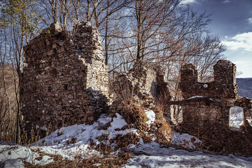 Ruiny zamku Sobień w Załużu oświetlone promieniami słońca, na tle drzew i błękitnego nieba z chmurami.