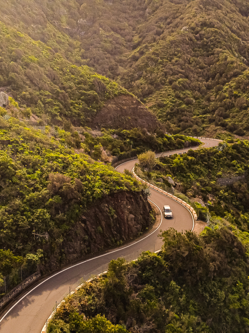 Fotografia przedstawia auto na drodze pełnej zakrętów, znajdującej się na zboczach gór Anaga. Północna Teneryfa.
Zdjęcie wykonane dronem.
