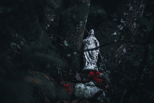 Niecodzienne ujęcie osamotnionej figurki religijnej w środku lasu.
