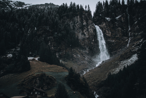 Zdjęcie wodospadu wypływającego z Alpejskiego zbocza. Wodospad znajduje się w centru malutkiej wioski.
