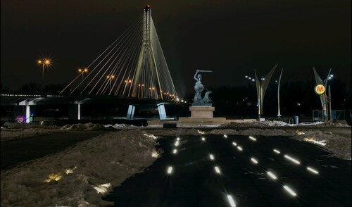 Ten widok uchwyciłem w połowie lutego 2021 roku. Zawiera 3 istotne symbole Warszawy: Most Świętokrzyski, nadwiślańską Syrenkę i symbol metra, przy zejściu do stacji Centrum Nauki Kopernik. Był późny wieczór, a po dłuższym postoju z pozoru niewielki mróz dawał się we znaki. Jednak sporo ludzi tamtędy przechodziło, więc musiałem nieco poczekać, by uzyskać 
