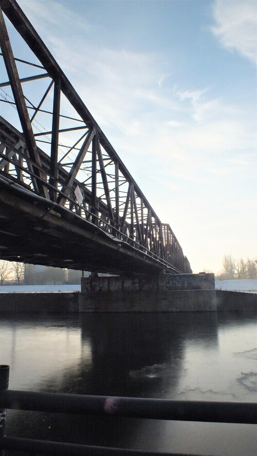 Zdjęcie przedstawia most kolejowy we Wrocławiu. Fotografia została zrobiona w pełnym świetle w zimowe popołudnie.