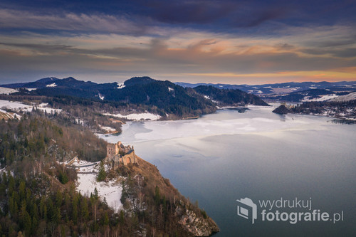 Fotografia przedstawia zamek Czorsztyn na pierwszym planie oświetlony promieniami zachodzącego słońca w jeden z zimowych dni 2020 roku. W tle można dostrzec zamek w Niedzicy 