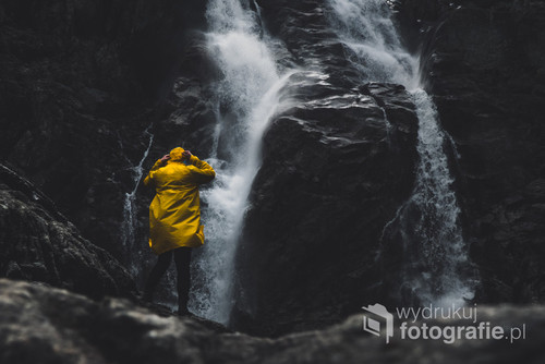 Osoba stojąca w żółtym płaszczu przeciwdeszczowym naprzeciwko wodospadu Siklawa w Polskich Tatrach.