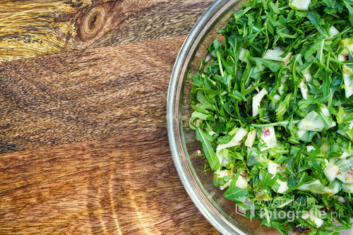 Glass bowl with green fresh salad on a wooden table. View from above.