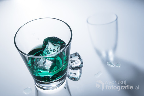A glass of green drink with ice on a glass table.