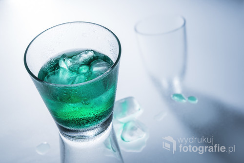 Glass of green drink with ice on a glass table.
