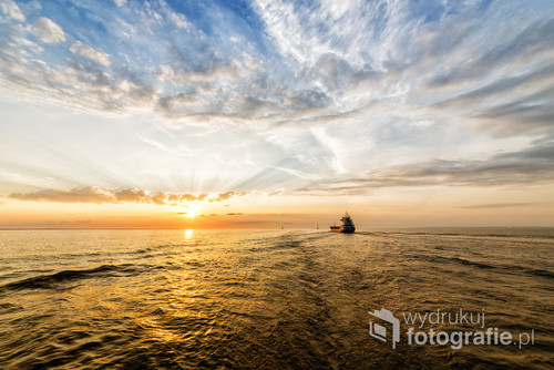 Amaizing Sunset. Empty container ship is sailing alonge the waterway during sunset. Small ship, colorfull sky and sea surface, dramatic blue dark sky. 