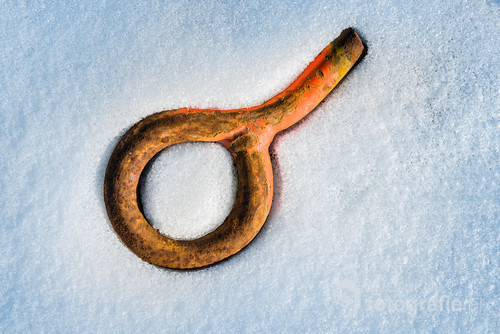 Old rusty bolt covered in frozen snow. View from above. Abstract image. Photo was taken during visit in old abandoned Polish Szczecin Shipyard.