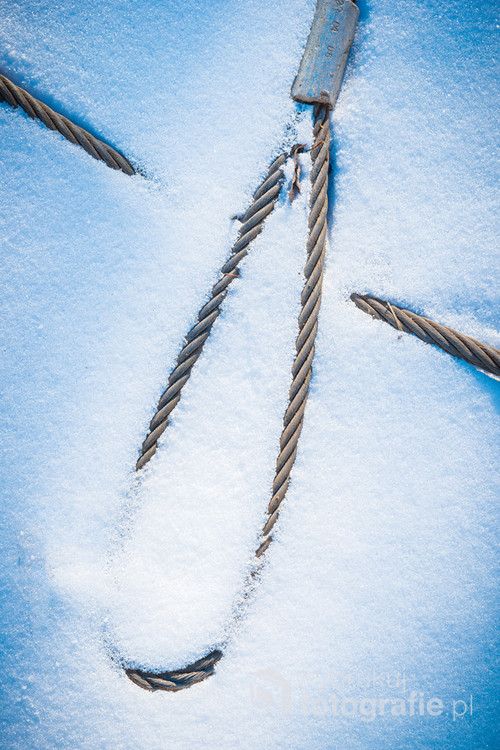 A steel, rusty rope covered in frozen snow. View from above. Abstract image. Photo was taken during visit in old abandoned Polish Szczecin Shipyard.