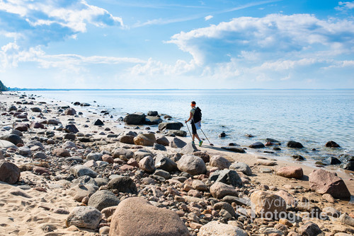A tourist walks along the stony shore of the Baltic Sea, doing Nordic walking.