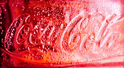 A glass With the Coca Cola logo, filled with carbonated drink. Dew drops on its surface.