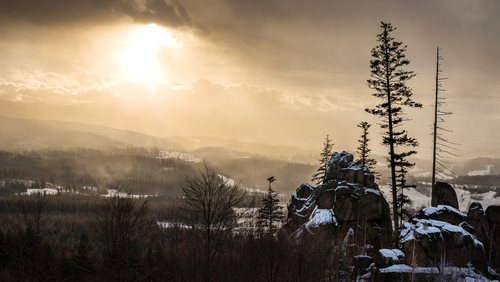 Zdjęcie wykonane zimowym późnym popołudniem i przedstawia (na pierwszym planie) Strużnickie Skały, w oddali w gęstych chmurach ukrywają się Karkonosze.