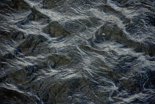 Sfotografowana została powierzchnia płynącej rzeki. Zdjęcie zostało nieco wyostrzone, a ponadto dodany został kolor niebieski.
