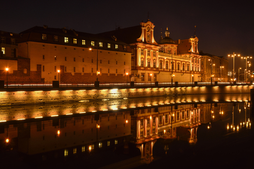 Fotografia przedstawia fragment centrum Wrocławia - rzeki Odry i budynku Ossolineum uchwyconych wieczorem.